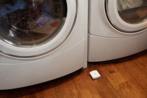 abode's water leak sensor placed on a hardwood floor next to a washing machine
